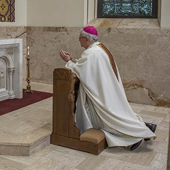 Bishop Ricken kneeling on a pew